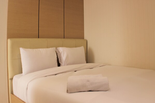 A neatly made bed with a folded towel, a headboard, and a wooden panel above it.