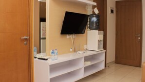 A hotel room with a white minibar, a flat-screen TV mounted on the wall, a water dispenser, and a door to the right. - Best Deal 2Br Apartment At Cinere Bellevue Suites (Depok)