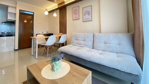 A modern living room with a sofa, a dining table with chairs, and a kitchen area in the background.
