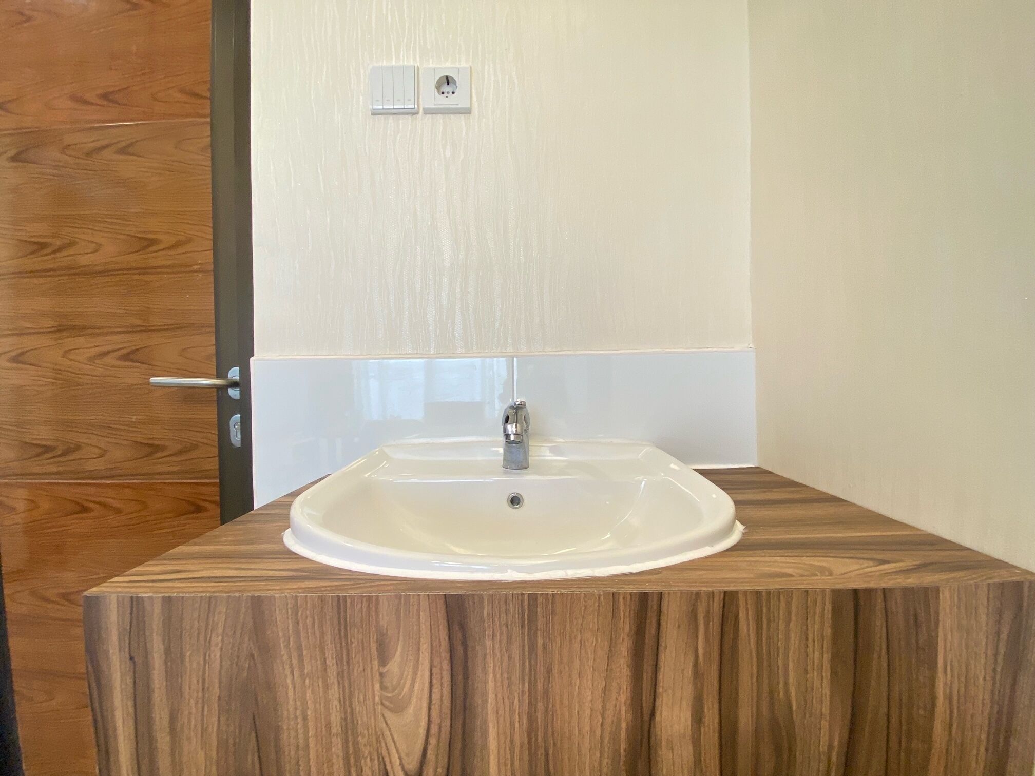 Een badkamer met een houten wastafelmeubel, een witte wastafel en een wandcontactdoos.
