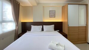A hotel room with a large bed, a wooden wardrobe, a bedside table, and a wall-mounted light.