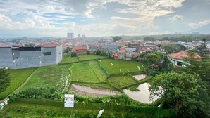 A rural landscape with a mix of agricultural fields and residential buildings, including a large white building and a smaller structure with a red roof. - Cozy Studio Room At Skyland City Jatinangor Apartment (Hegarmanah)