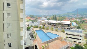 A high-rise building with a rooftop swimming pool and a view of a cityscape with mountains in the background. - Cozy Studio Room At Skyland City Jatinangor Apartment (Hegarmanah)