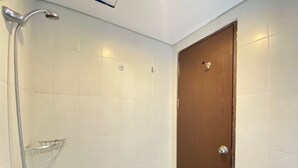 A small, tiled bathroom with a shower, a wooden door, and a towel rack. - Cozy Studio Room At Skyland City Jatinangor Apartment (Hegarmanah)