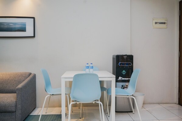 A small, clean room with a white table, two blue chairs, a grey sofa, and a water dispenser.