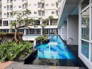 Une piscine d’une profondeur de 120 cm, entourée de verdure et de bâtiments modernes.