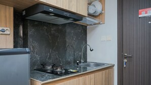 A compact kitchen with a black marble backsplash, wooden cabinets, a stainless steel sink, and a built-in stove.