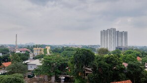 A high-rise building with multiple floors, surrounded by dense greenery and other residential buildings.