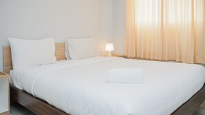 A neatly made bed with white linens, a wooden headboard, and a bedside lamp.