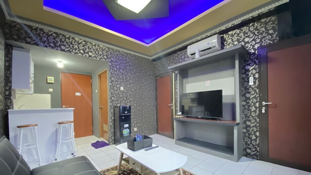 Ein Wohnzimmer mit einer Couch, einem Couchtisch, einem Fernseher und einer Küchenzeile inklusive Kühlschrank und Mikrowelle.