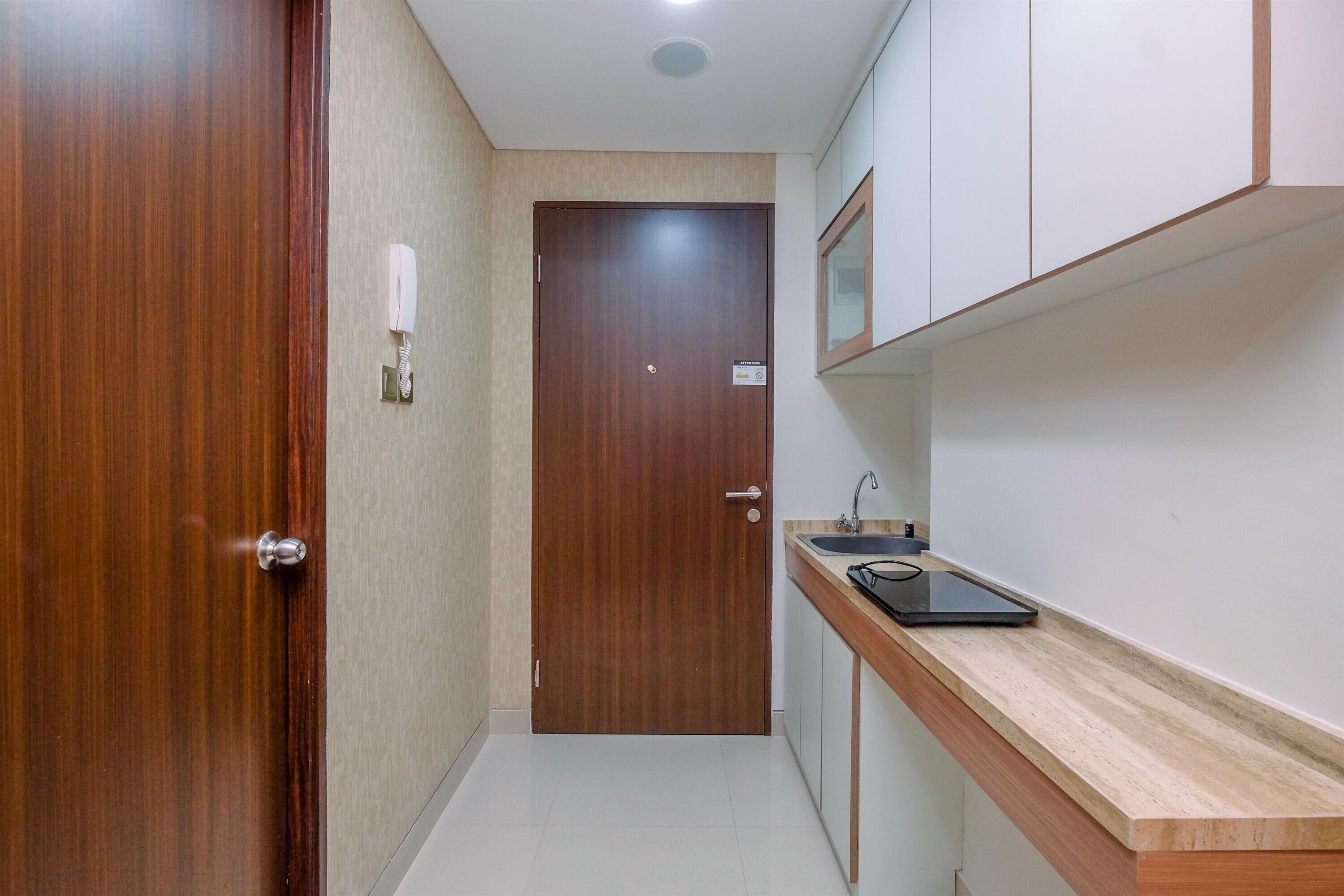 Un couloir étroit avec une porte en bois, un petit lavabo avec un miroir et un plan de travail.