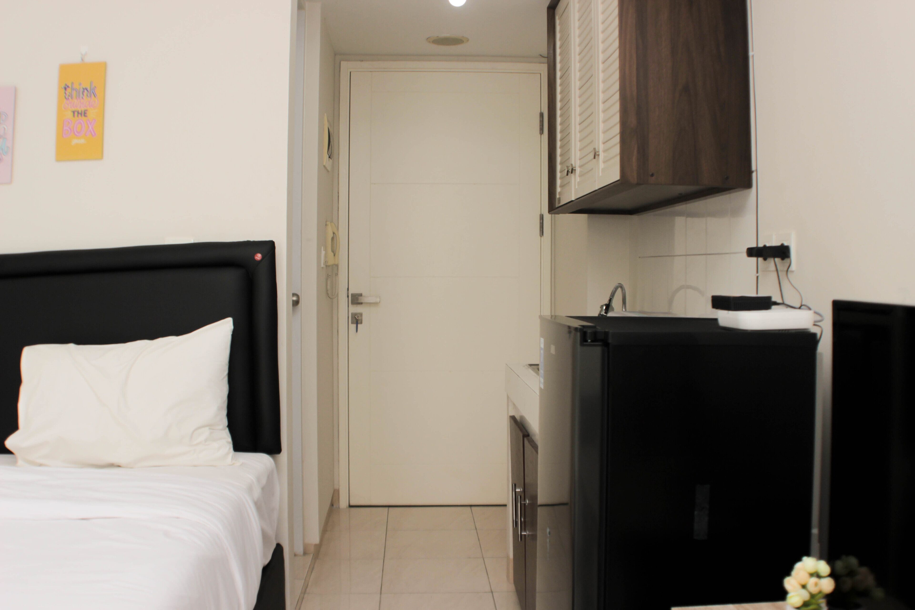 A bedroom with a bed, a small kitchenette, and a door leading to another room.