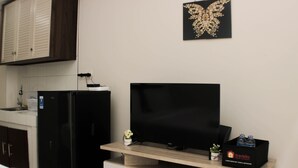 Una kitchenette compacta con un refrigerador negro, un microondas y un lavamanos. Un televisor de pantalla plana está montado en un estante de madera sobre la encimera.