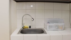 Una cocina con un lavamanos de acero inoxidable, armarios blancos y salpicadero de azulejos blancos.