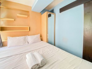 Un lit bien fait, avec des draps blancs et des serviettes pliées, une tête de lit en bois et un mur bleu clair.