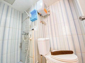 Une salle de bain avec des murs recouverts de carreaux à rayures, des toilettes, une douche et une boîte de rangement bleue.