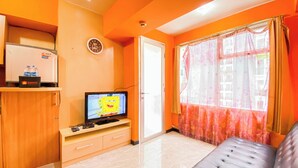 A room with a TV displaying a cartoon, a sofa, a cabinet with a water dispenser, and a window with curtains. - Homey Living 2Br At Jarrdin Cihampelas Apartment (Bandung)