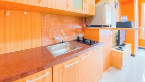 A kitchen with wooden cabinets, a stainless steel sink, and a gas stove. - Homey Living 2Br At Jarrdin Cihampelas Apartment (Bandung)