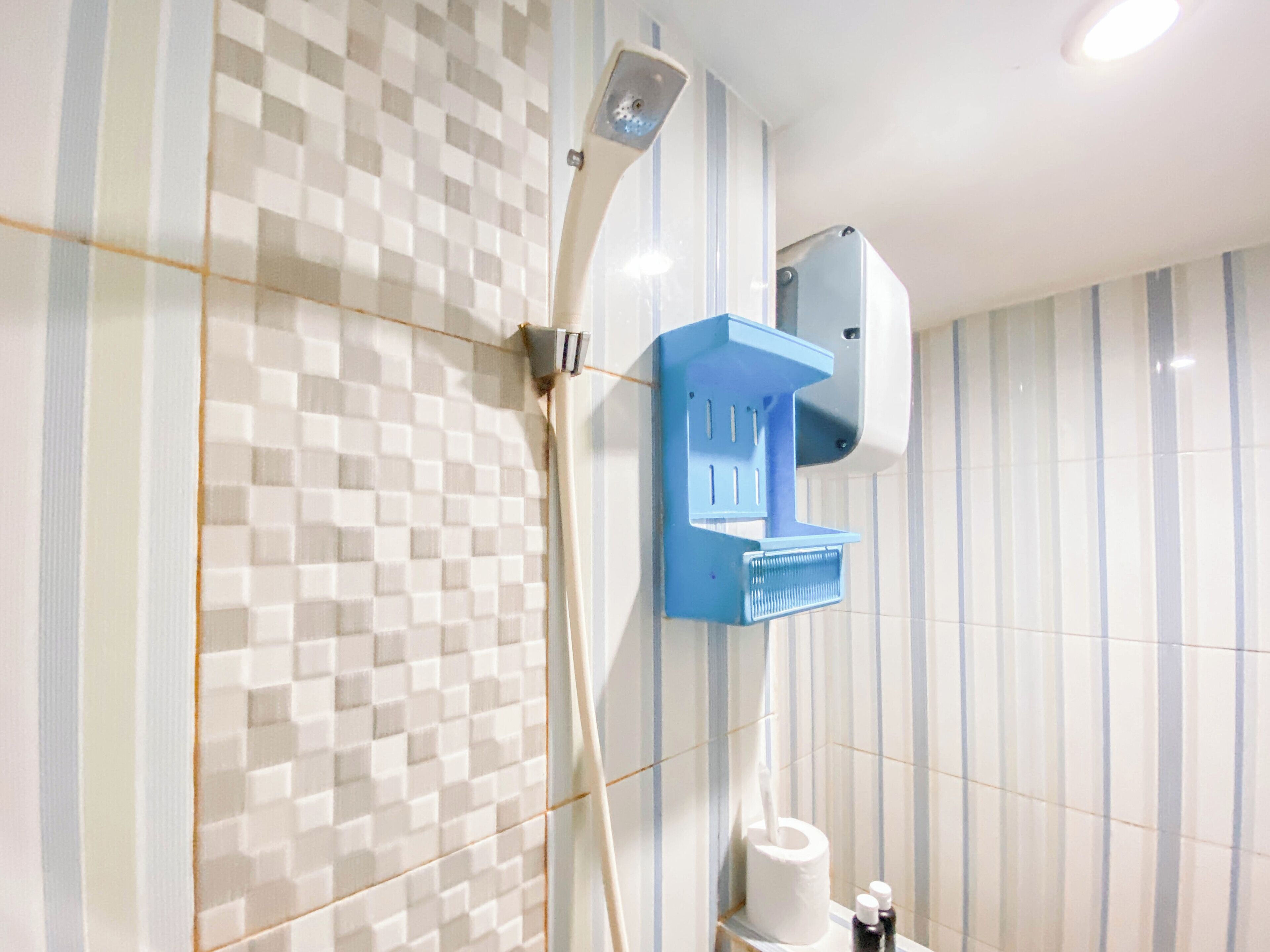 Un baño con pared de baldosas a cuadros, ducha con panel de control azul y dispensador de papel higiénico.