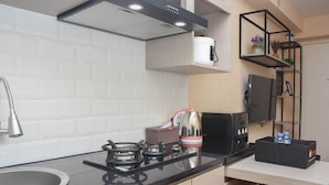 A modern kitchen with a black countertop, stainless steel sink, and a built-in range hood. - Enjoy Living And Tidy 1Br Bassura City Apartment (Jakarta)