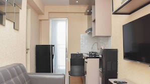 A compact living space with a sofa, a small kitchen area, a refrigerator, a TV, and a chair. - Enjoy Living And Tidy 1Br Bassura City Apartment (Jakarta)