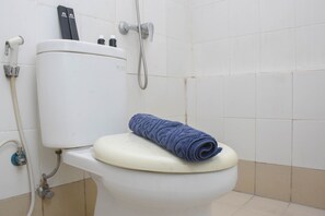 A toilet with a blue towel on the seat, a showerhead, and a water heater. - Cozy Stay And Comfort 2Br At Bassura Apartment (Jakarta)