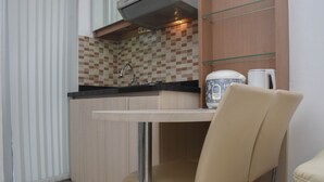 A compact kitchen with a tiled backsplash, a stainless steel sink, and a white kettle on the counter.