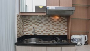 A compact kitchen with a black countertop, a stainless steel sink, a gas stove, a coffee maker, and a microwave.