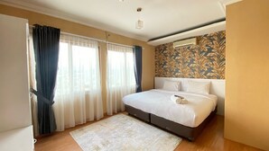 A bedroom with a bed, curtains, a patterned rug, and a wall with a leaf design. - Cozy Furnished 3Br At Grand Setiabudi Apartment (Bandung)