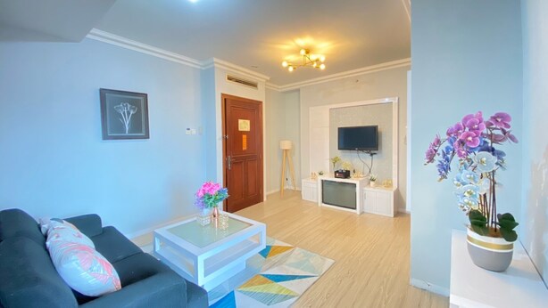 A living room with a sofa, coffee table, and a TV in the background. - Cozy Furnished 3Br At Grand Setiabudi Apartment (Bandung)