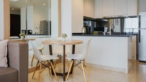 A modern kitchen with white cabinets, a central island with seating, and a dining area with a round table and chairs. - Well Designed And Cozy 2Br Apartment Branz Bsd City (Pagedangan)