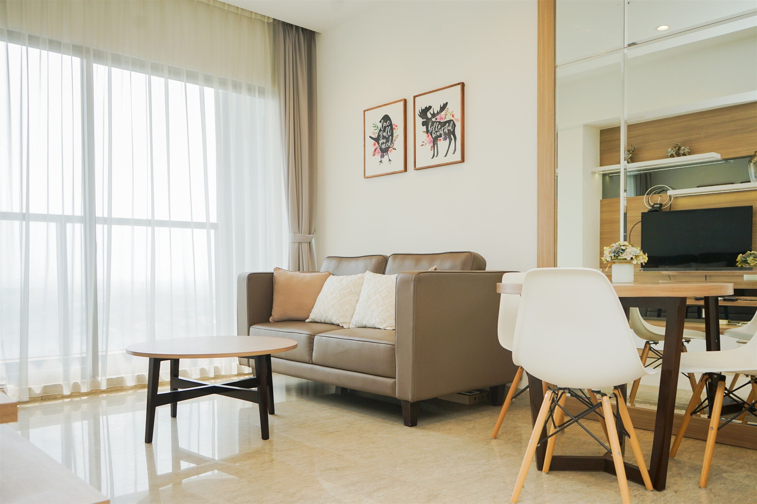 A modern living room with a sofa, a dining table, and chairs. There are two framed pictures on the wall.