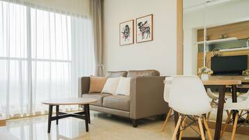 A modern living room with a sofa, a dining table, and chairs. There are two framed pictures on the wall.