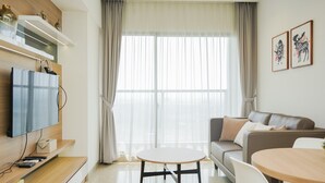 A modern living room with a flat-screen TV, a round dining table, a sofa, and a large window with sheer curtains. - Well Designed And Cozy 2Br Apartment Branz Bsd City (Pagedangan)