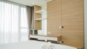 A modern hotel room with a large bed, a wooden wardrobe, a built-in desk, and a large window with sheer curtains. - Well Designed And Cozy 2Br Apartment Branz Bsd City (Pagedangan)