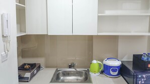 A kitchen with a stainless steel sink, a gas stove, a green electric kettle, and a blue rice cooker. - Nice And Homey 2Br At Vida View Makasar Apartment (Makassar)