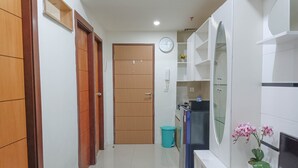 A hallway with wooden doors, a clock, a trash bin, a refrigerator, and a potted orchid. - Nice And Homey 2Br At Vida View Makasar Apartment (Makassar)