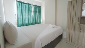 A bedroom with a bed, a wardrobe, and a window with curtains. - Nice And Homey 2Br At Vida View Makasar Apartment (Makassar)