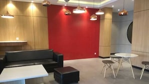 A modern lobby with a red accent wall, black leather seating, a white coffee table, and a round table with four chairs. - Well Designed Studio Apartment At Taman Melati Jatinangor (Hegarmanah)