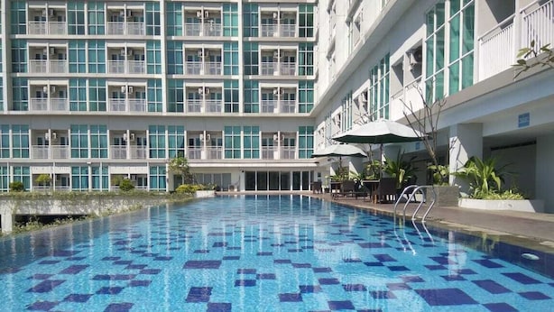 A swimming pool with a checkered pattern, surrounded by a building with balconies and a covered seating area. - Well Designed Studio Apartment At Taman Melati Jatinangor (Hegarmanah)