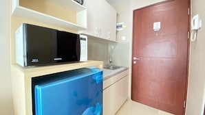 A kitchen with a microwave, a refrigerator, a sink, and a wooden door. - Well Designed Studio Apartment At Taman Melati Jatinangor (Hegarmanah)