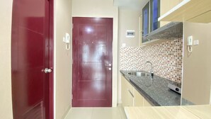 A compact kitchen with a red door, a tiled backsplash, and a stainless steel sink. - Cozy Studio Corner Room At Taman Melati Jatinangor Apartment (Hegarmanah)
