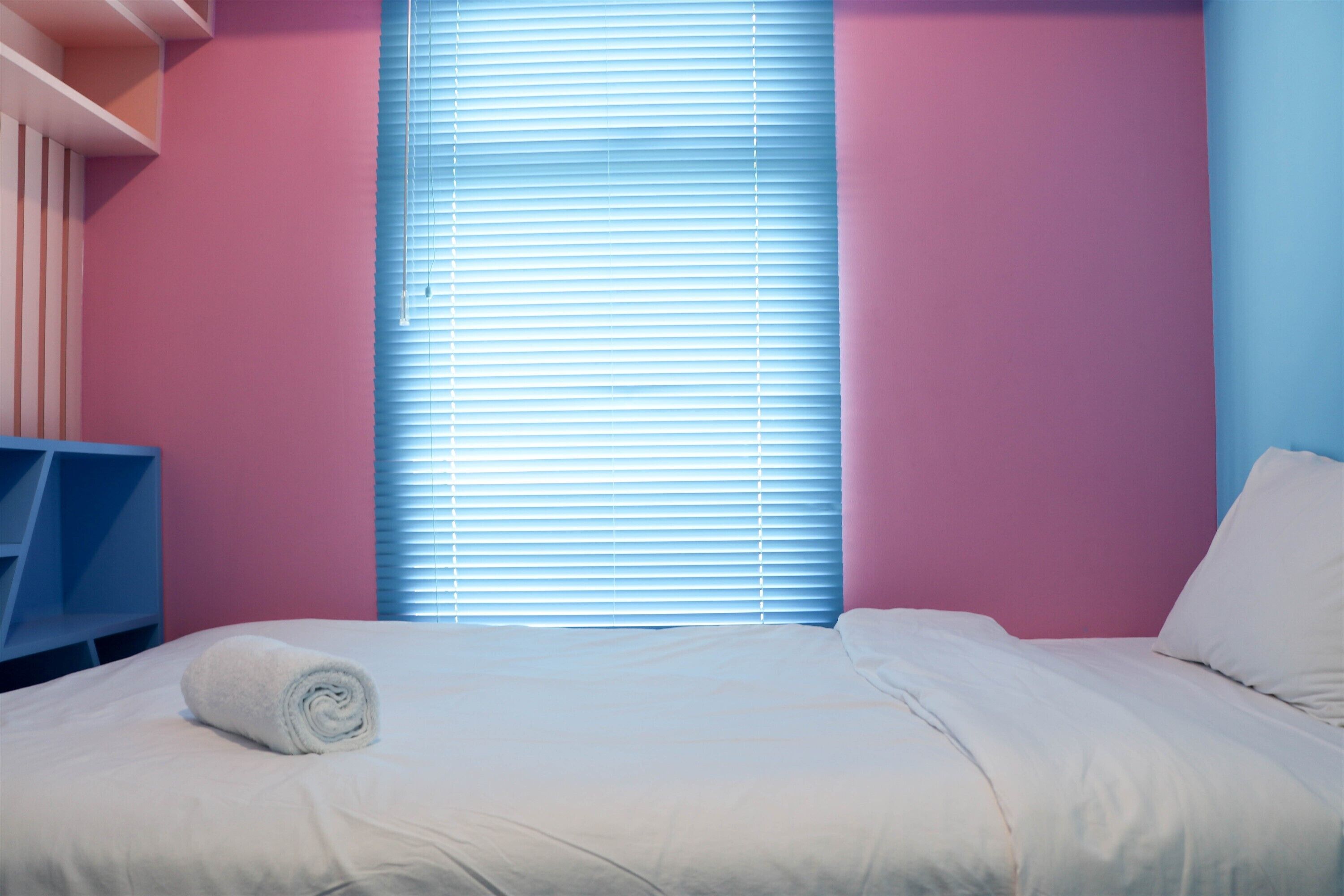 Een slaapkamer met een bed, een opgerolde handdoek en een raam met zonwering.