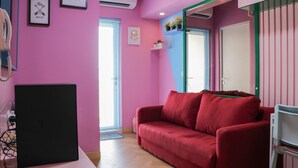 A room with pink walls, a red sofa, a black TV, and a white chair. - Comfort And Cozy 2Br At Springlake Summarecon Bekasi Apartment (Bekasi)