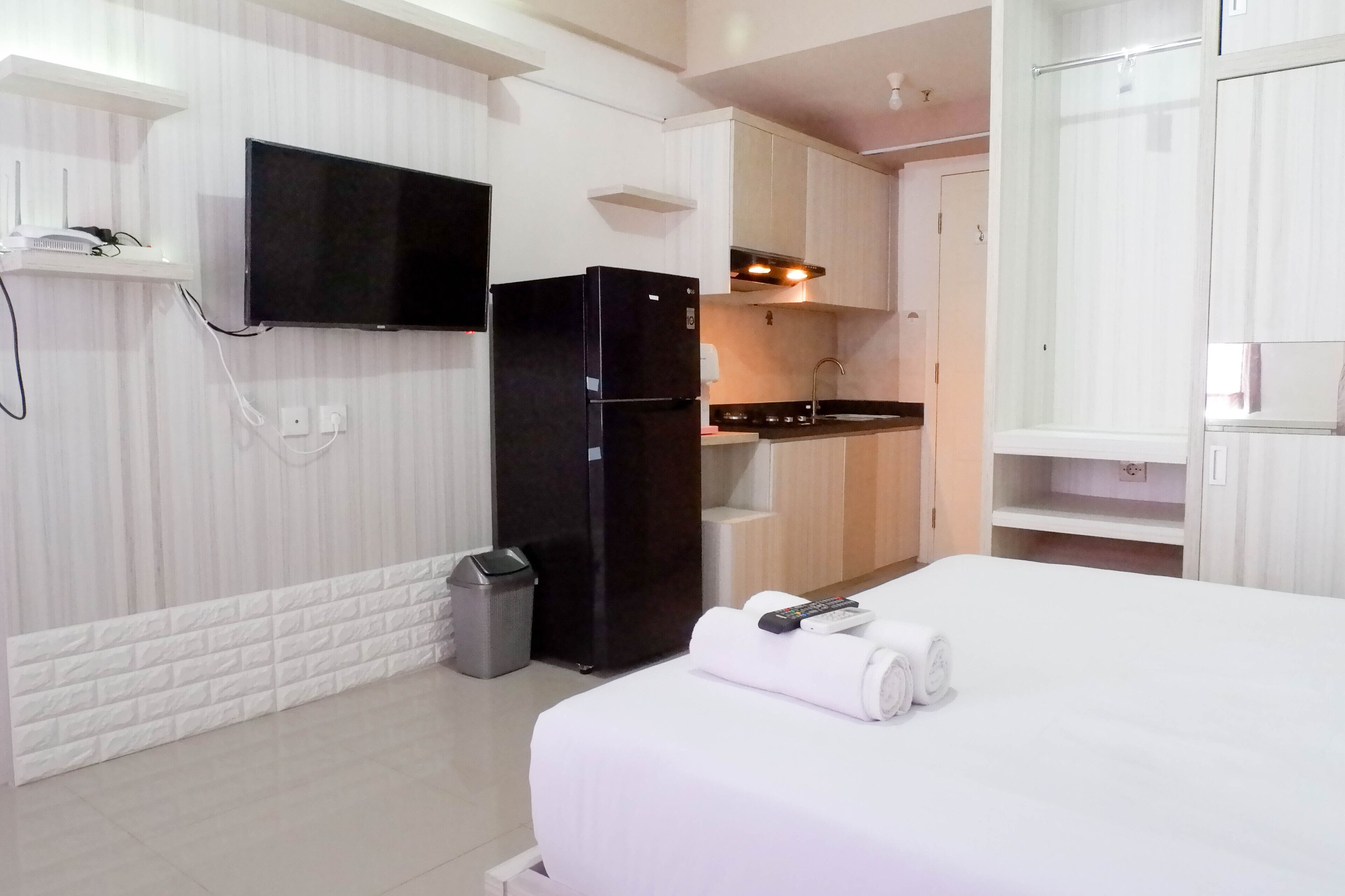 A hotel room with a bed, a TV mounted on the wall, a refrigerator, a sink, and a small kitchen area.