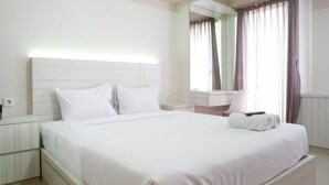 A neatly made bed with white bedding, a bedside table, a mirror, and a window with curtains. - Spacious Studio Apartment Accses To Pakuwon Mall At Tanglin Supermall Mansion (Surabaya)