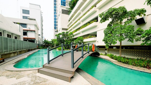 Ein moderner, überdachter Pool mit Holzdeck und Metallgeländern, umgeben von viel Grün und angrenzend an ein Mehrstöckiges Gebäude mit Balkonen.