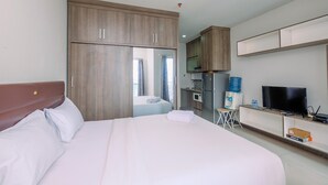 A hotel room with a large bed, a wardrobe, a TV, a mini-fridge, and a water dispenser.