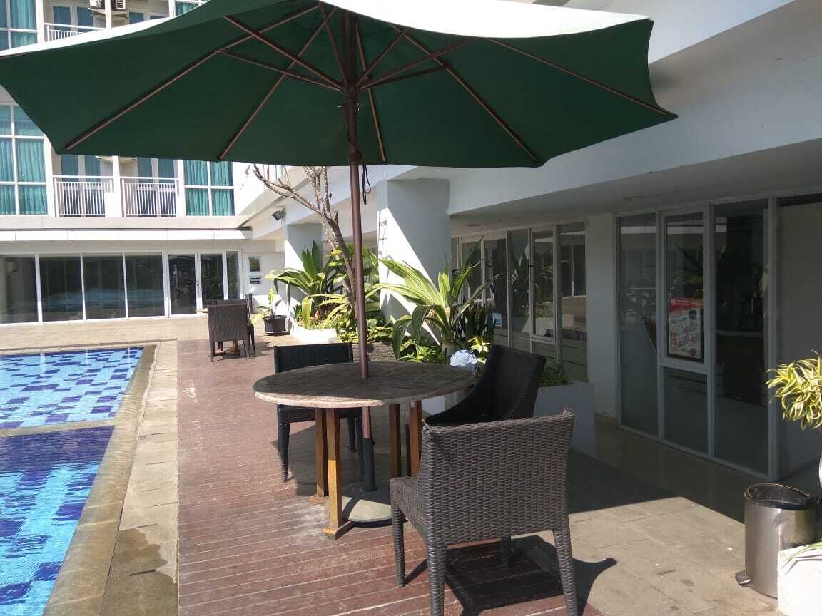 Un área junto a la piscina con una mesa redonda, sillas y una sombrilla grande.