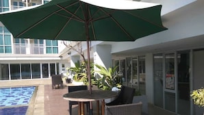 Un espace aménagé au bord de la piscine, avec une table ronde, des chaises et un grand parasol.